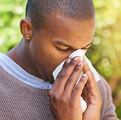 Shot of a young man with environmental allergy blowing his nose outdoors
