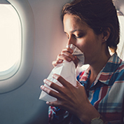 Young woman suffering from motion sickness during a flight and breathing in vomit bag
