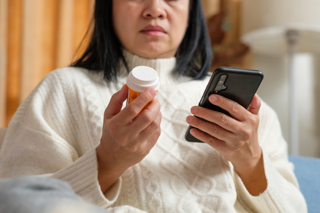 asian woman reading pill prescription on mobile when get flu on sofa at home